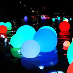 many different colored balls floating in the water at night with lights reflecting off them on the surface