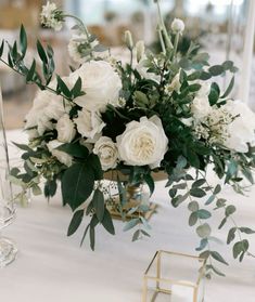 white flowers and greenery are arranged in a vase on a table with candlesticks