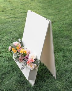 a white sign with flowers on it in the grass