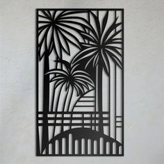 a metal wall hanging with palm trees and buildings in the background on a white wall