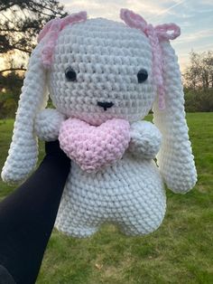 a crocheted bunny holding a pink heart in it's hand on the grass