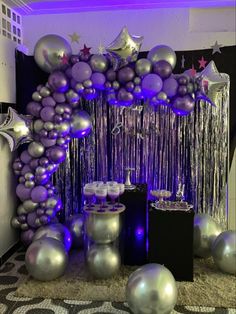 purple and silver balloons are hanging from the ceiling in front of a party arch with streamers