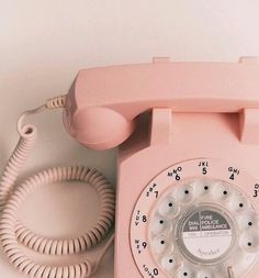 an old pink phone sitting on top of a white wall next to a telephone cord