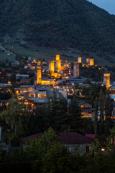 the city is lit up at night with mountains in the background