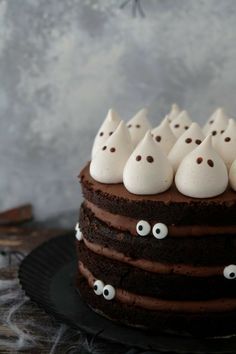 a chocolate cake with white frosting and ghost eyes on top, sitting on a black plate