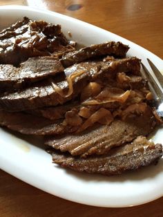 a white plate topped with sliced up meat and a fork on top of a wooden table