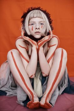 a woman with painted body art sitting on a bed in front of an orange background