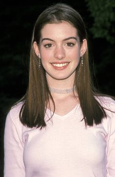 a woman with long brown hair wearing a white shirt and diamond earrings smiling at the camera