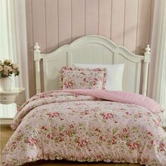 a white bed with pink and green floral comforter set on it's side