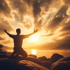 a man sitting on top of a rock next to the ocean with his arms wide open