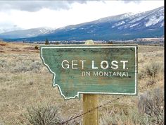 a wooden sign that says get lost in montana with mountains in the backgroud