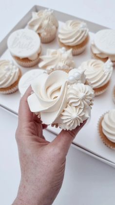 a hand is holding a cupcake with white frosting and flowers on the top