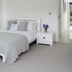 a white bed sitting next to a window in a bedroom on top of a carpeted floor