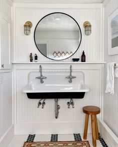 a white sink sitting under a round mirror in a bathroom next to a wooden stool