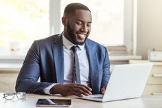 a man sitting at a table with a laptop computer in front of him and smiling