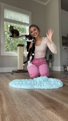 a woman in pink pants holding a black and white cat on top of a wooden floor