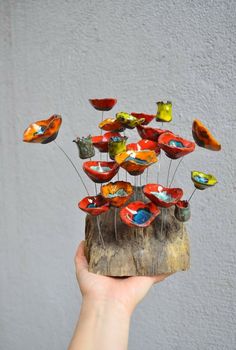 a hand holding up a small tree stump with colorful glass birds on it