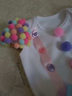 a white shirt with pink, blue and yellow pom - poms on it