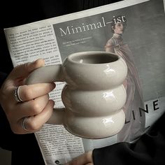 a person holding a coffee mug in their hand while reading a magazine about minimalist