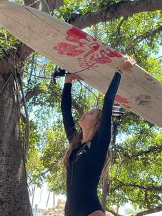 a woman in a black bodysuit holding a surfboard above her head and looking up at the sky