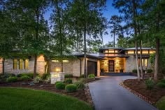 a house with lots of trees and grass in front of it at night, lit up by lights on the windows