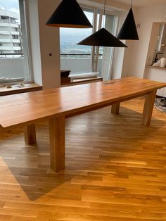 a large wooden table with three black lamps hanging from it's sides in an apartment