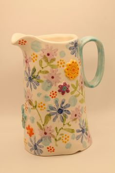 a ceramic pitcher with flowers painted on the front and sides, sitting against a white background