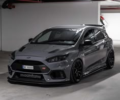 a grey car parked in a parking garage next to a white wall and red light