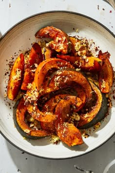 a white bowl filled with cooked squash and nuts on top of a table next to utensils