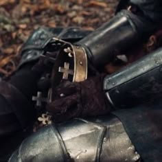 a close up of a person's foot wearing armor and holding a cross on the ground