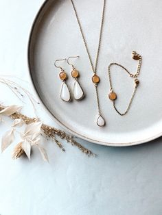 three pieces of jewelry sitting on top of a white plate next to some dried flowers