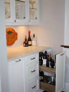 a kitchen with white cabinets and wine bottles in the cupboards on the counter top