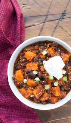 a white bowl filled with chili and sweet potato stew on top of a wooden table