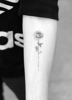 a black and white photo of a single rose tattoo on the left inner arm,