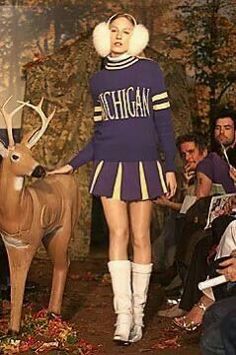 a woman in a cheerleader outfit standing next to a deer