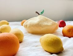 an assortment of fruit on a bed with white linens and a knitted bag