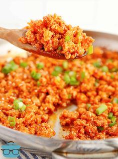 a spoon full of food that is being lifted from a casserole dish with rice and green onions