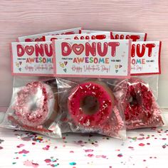 three donuts are wrapped in plastic and have pink sprinkles