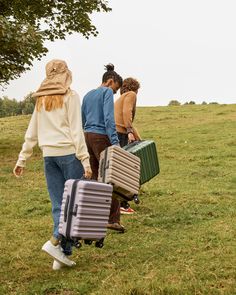 four people carrying suitcases down a grassy hill