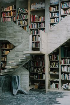 a room with several bookshelves filled with lots of books next to a stair case