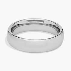 a white gold wedding ring on a plain surface, with a rounded design and high polished edges