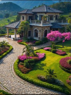 an aerial view of a large house surrounded by lush green trees and bushes with pink flowers in the foreground