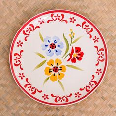 a plate with flowers painted on it sitting on a woven tablecloth covered floor next to a basket