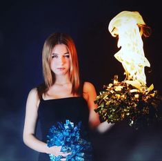 a woman in a black dress holding a blue and white bouquet with flames behind her