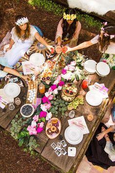 people are sitting at a table with plates and flowers on it, surrounded by food