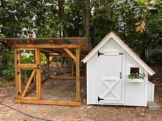 a small white shed sitting next to a wooden structure in the middle of a forest