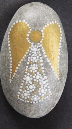 a rock with an angel painted on it and some white dots in the middle, sitting on a black surface