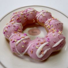 a pink donut with white frosting and sprinkles on a plate