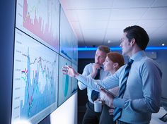 three people standing in front of a white board with graphs on it and pointing to them