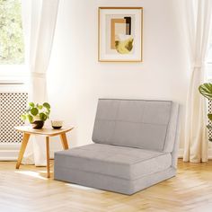 a living room with white walls and wooden floors, a gray chair in front of a window